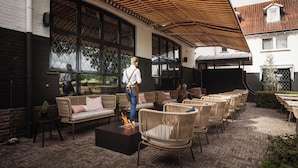 An outdoor seating area with wicker furniture, a fire feature, and a covered patio. - Paping Hotel & Spa by Flow (Ommen)