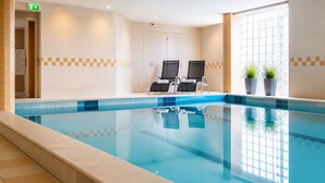 An indoor swimming pool with two lounge chairs, a door, and a window with plants. - Paping Hotel & Spa by Flow (Ommen)