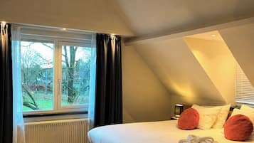 A bedroom with a large bed, a window with curtains, a radiator, and a wooden floor.