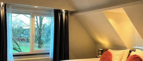 Un dormitorio con una cama grande, una ventana con cortinas, un radiador y suelo de madera.