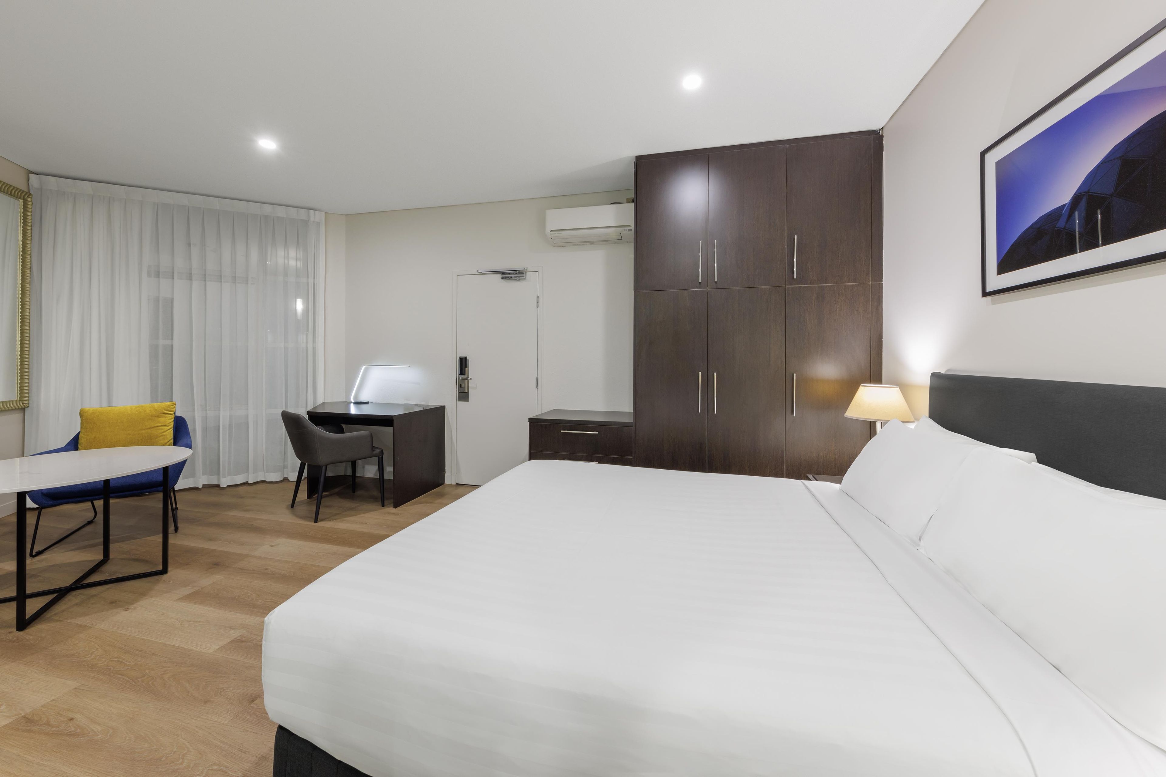 Habitació d'hotel amb llit, escriptori, cadira, armari i un quadre a la paret.