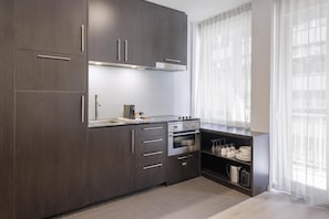Una cocina moderna con armarios de madera oscura, electrodomésticos de acero inoxidable y un ventanal con cortinas de gasa.