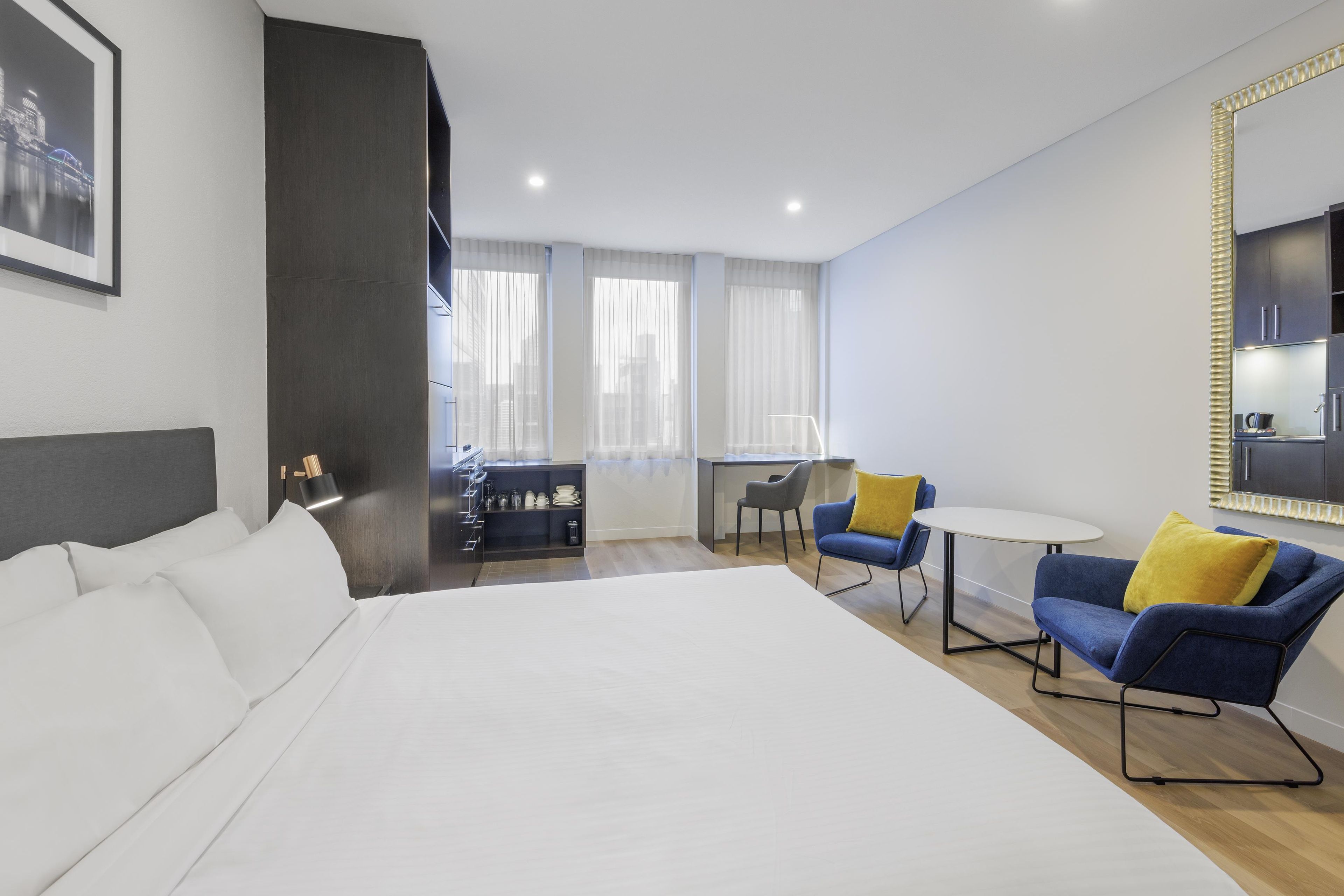 A modern hotel room with a large bed, a desk, two chairs, and a dining table.