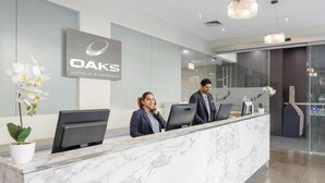 Un mostrador de recepción con encimera de mármol, un cartel de OAKS Hotels & Resorts y una orquídea en maceta.