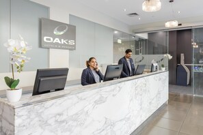 Un mostrador de recepción con encimera de mármol, un cartel de OAKS Hotels & Resorts y una orquídea en maceta.