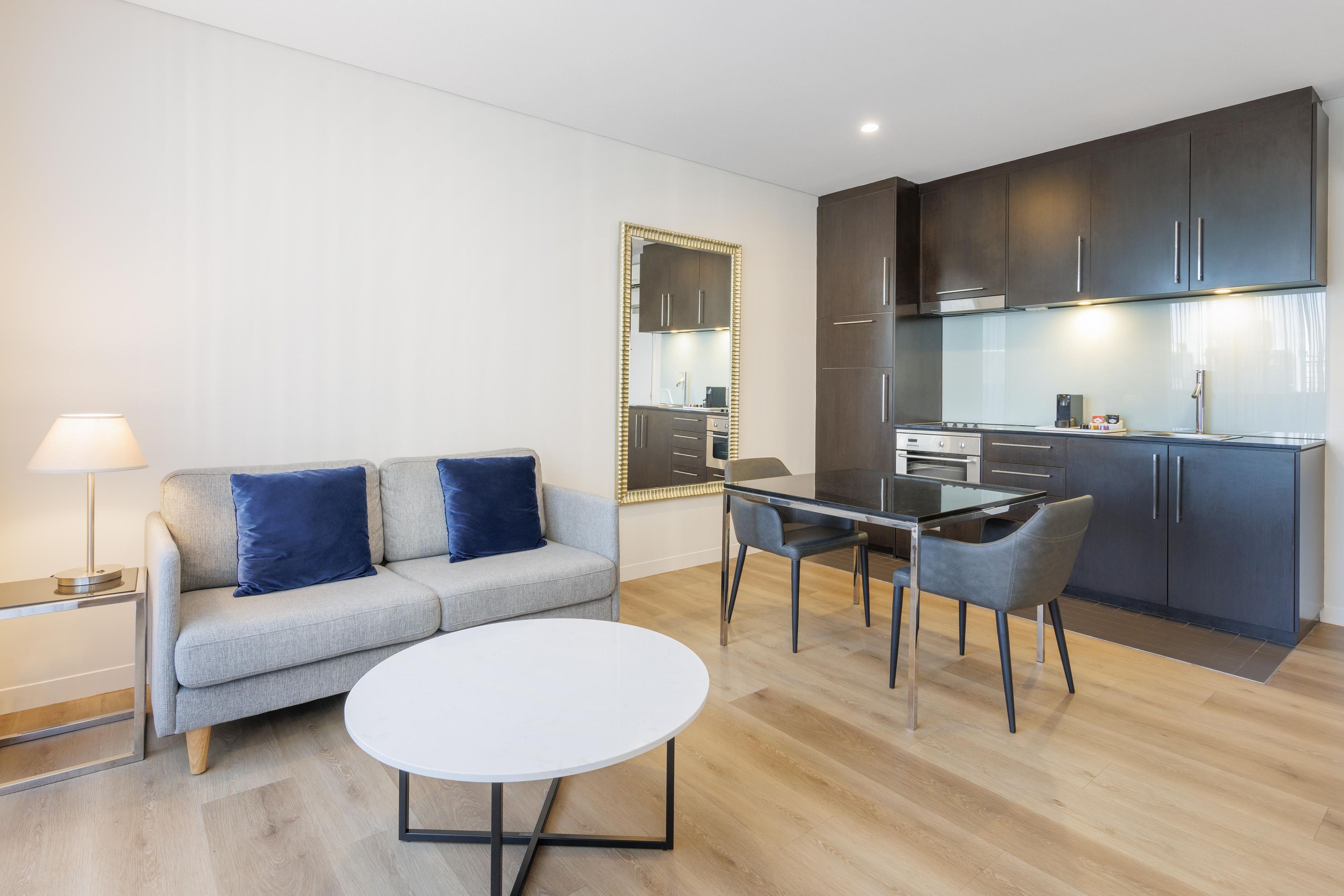 A modern living room with a sofa, a round table, and a kitchen area with cabinets and appliances.