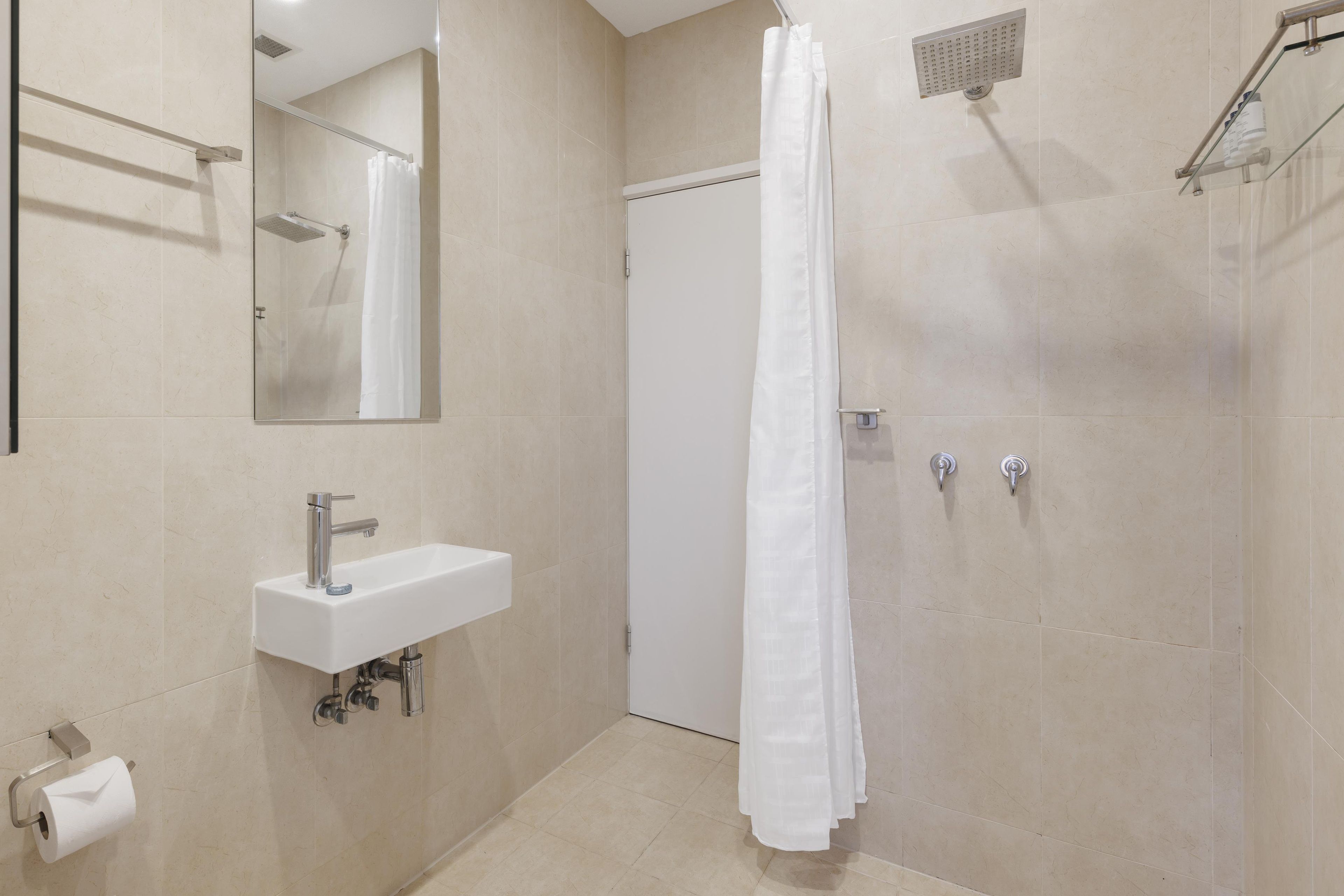A bathroom with a sink, mirror, shower, and toilet paper.