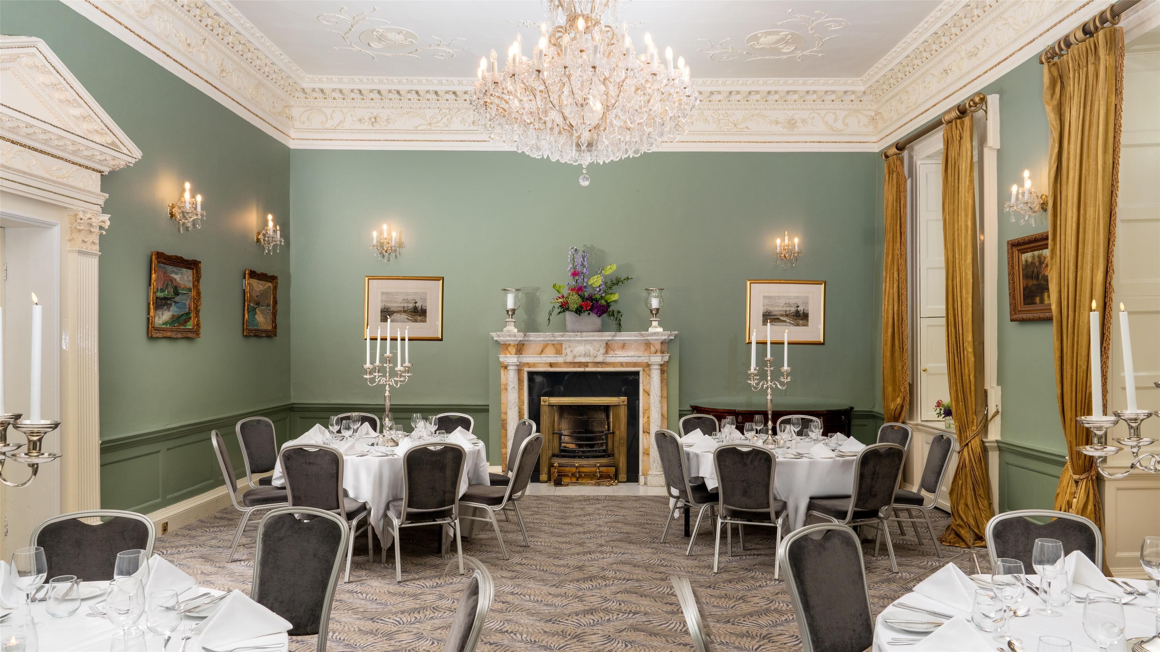 A formal dining room with a fireplace, chandeliers, and framed artwork on the walls.