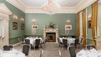 A formal dining room with a fireplace, chandeliers, and framed artwork on the walls.