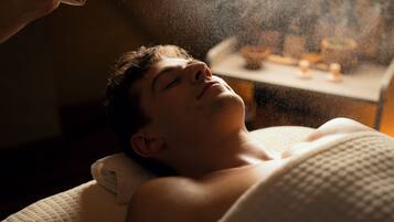 A person lying down, possibly in a spa or treatment room, with a table and some items in the background.