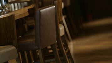 A restaurant interior with wooden tables and chairs, dim lighting, and a dark ambiance.