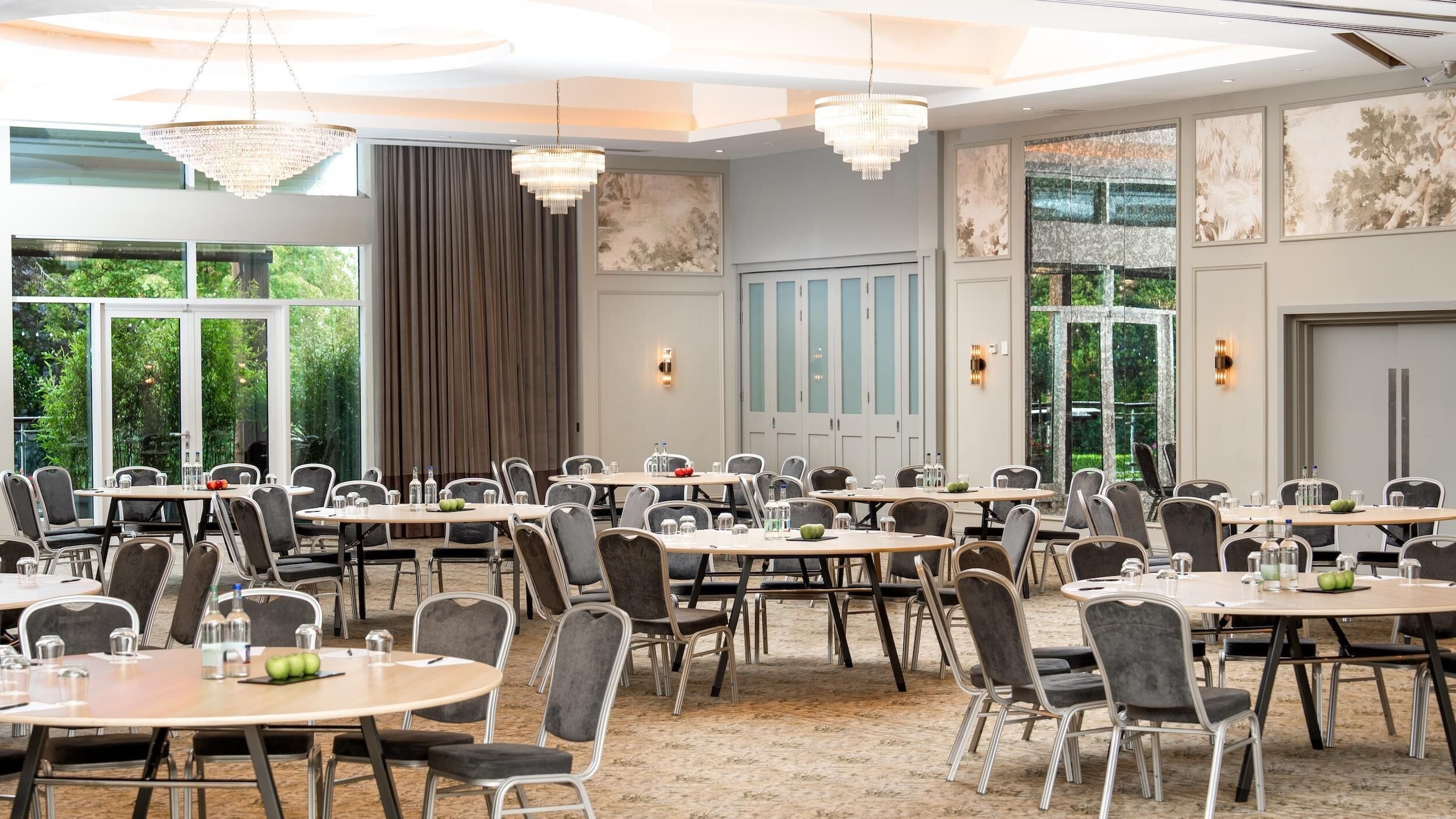 Un salón de conferencias con varias mesas y sillas, ventanas amplias y candelabros.