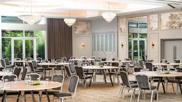 Un salón de conferencias con varias mesas y sillas, ventanas amplias y candelabros.
