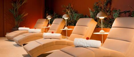 A row of beige lounge chairs with white towels and red flowers, each with a small table and a lamp.