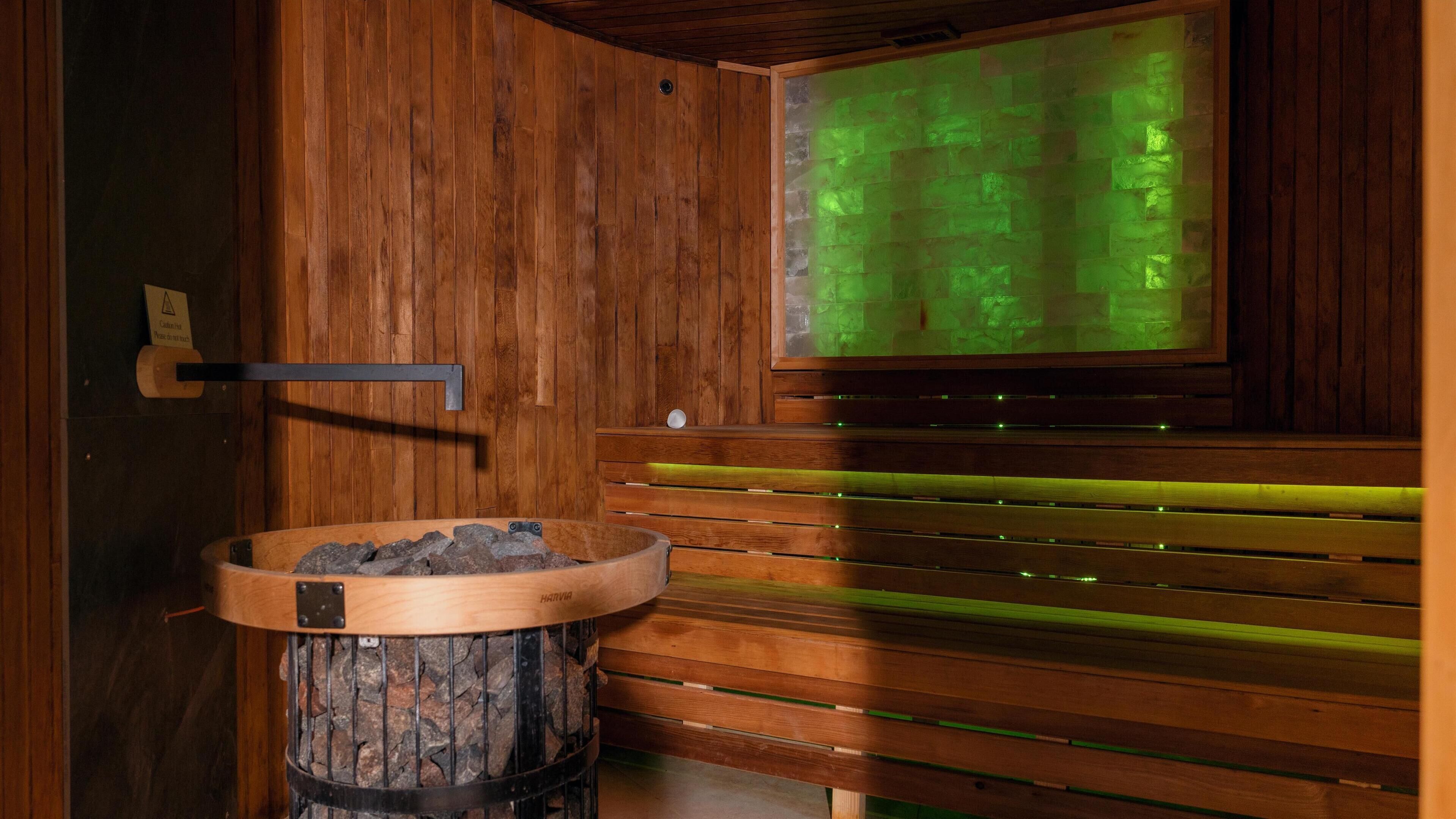 Eine Sauna mit Holzbänken, einem Steingefäß und einer grüngenierten Wand.