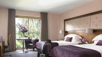 Ein Hotelzimmer mit zwei Betten, einer Sitzecke mit Tisch und Stuhl sowie Blick auf Bäume durch das Fenster.