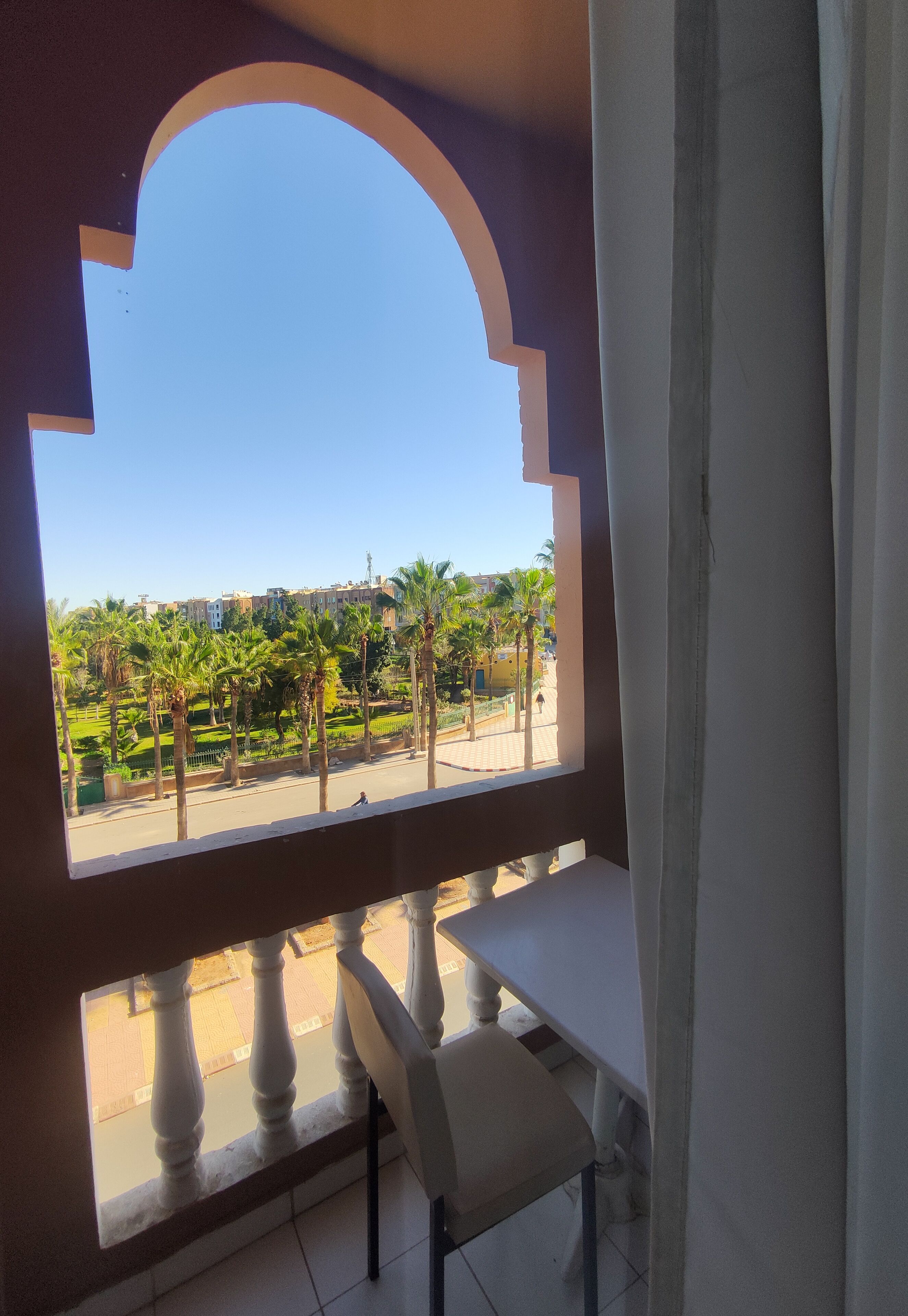 Un balcón con vistas a una zona ajardinada con palmeras y edificios al fondo.