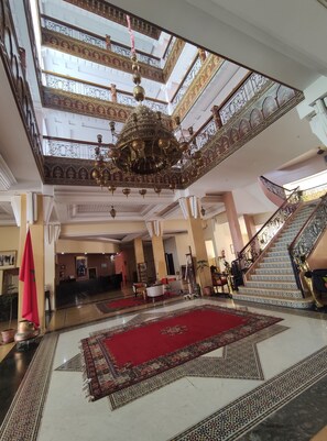 Un'imponente hall con soffitto alto, lampadari decorati, un tappeto rosso e una scalinata con ringhiere elaborate.
