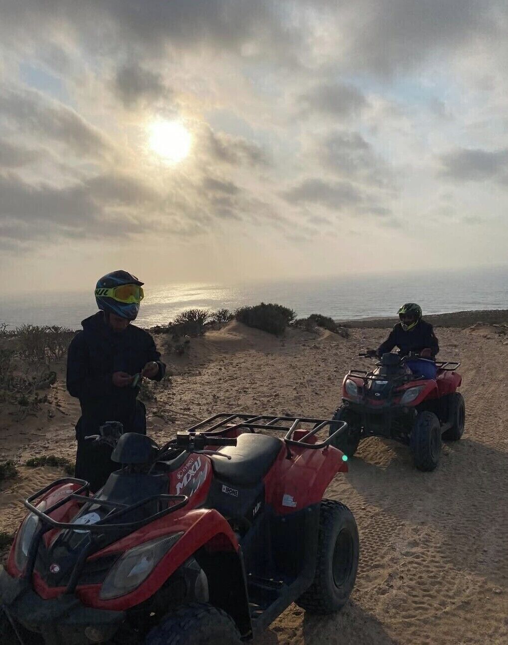 Two ATVs on a sandy path with a beach and ocean in the background.
