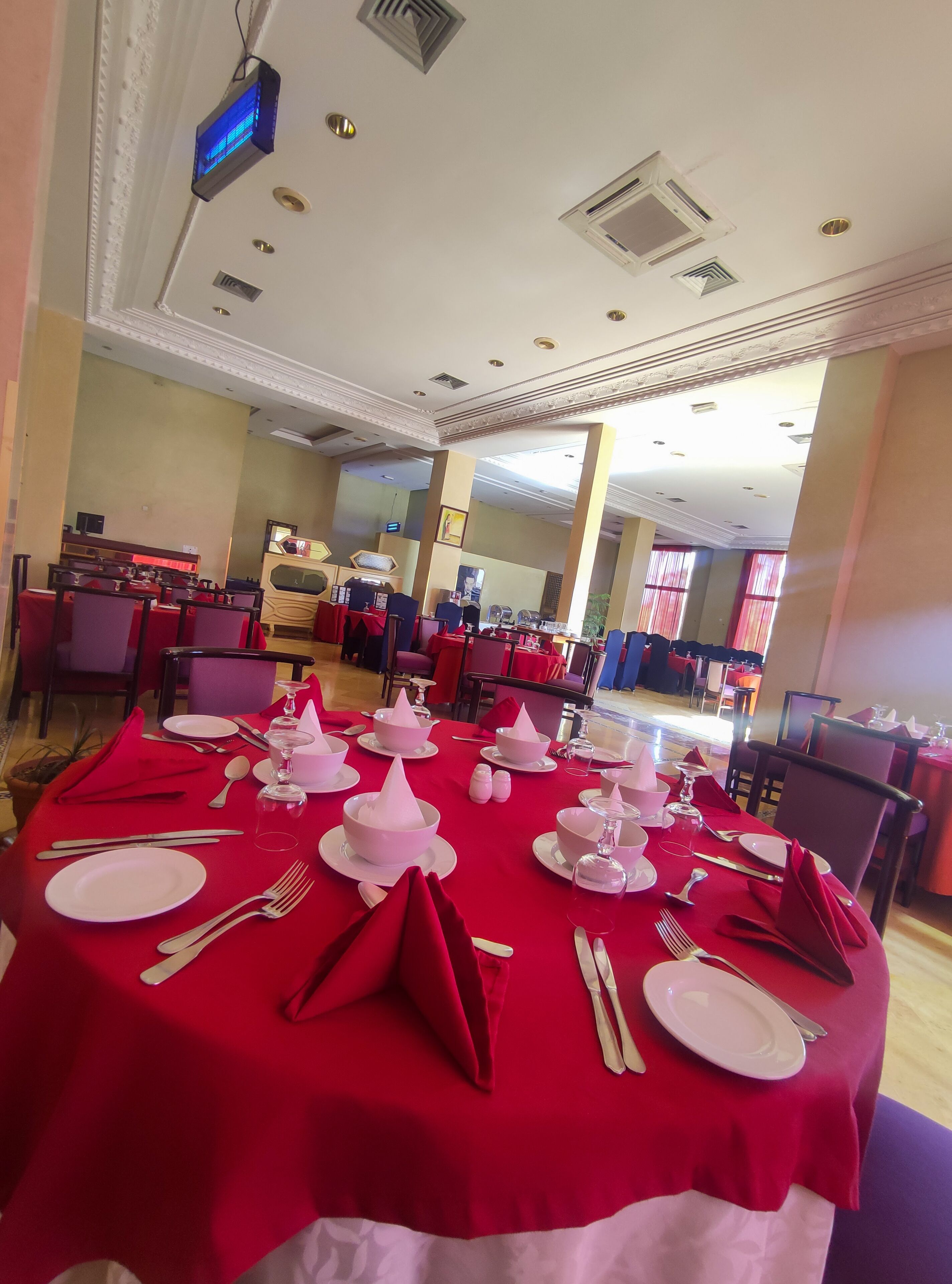Un comedor con mesas dispuestas para una comida formal, con platos blancos, cubiertos y servilletas rosas.