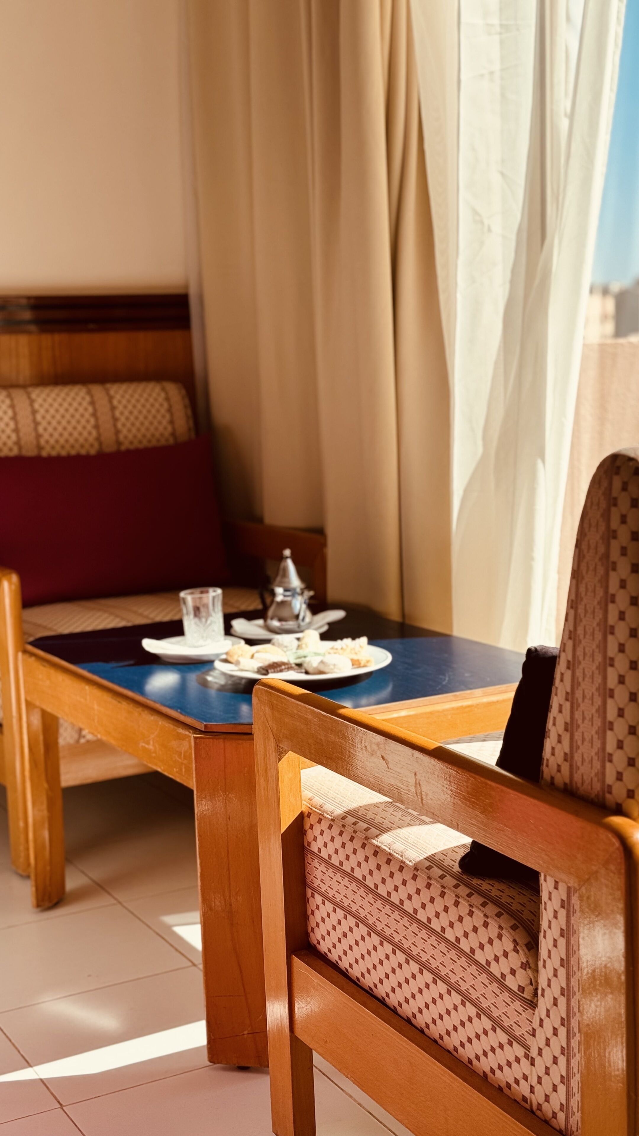 A dining area with a wooden table and chairs, a teapot, and a plate of pastries.