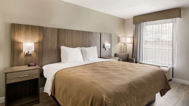 A hotel room with a large bed, bedside tables with lamps, a nightstand, and a window with curtains. - Quality Inn Emporia (Emporia)