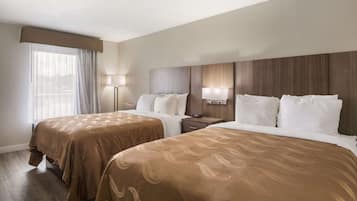 Quarto de hotel com duas camas, uma janela grande com cortinas, abajures e cabeceira de madeira.