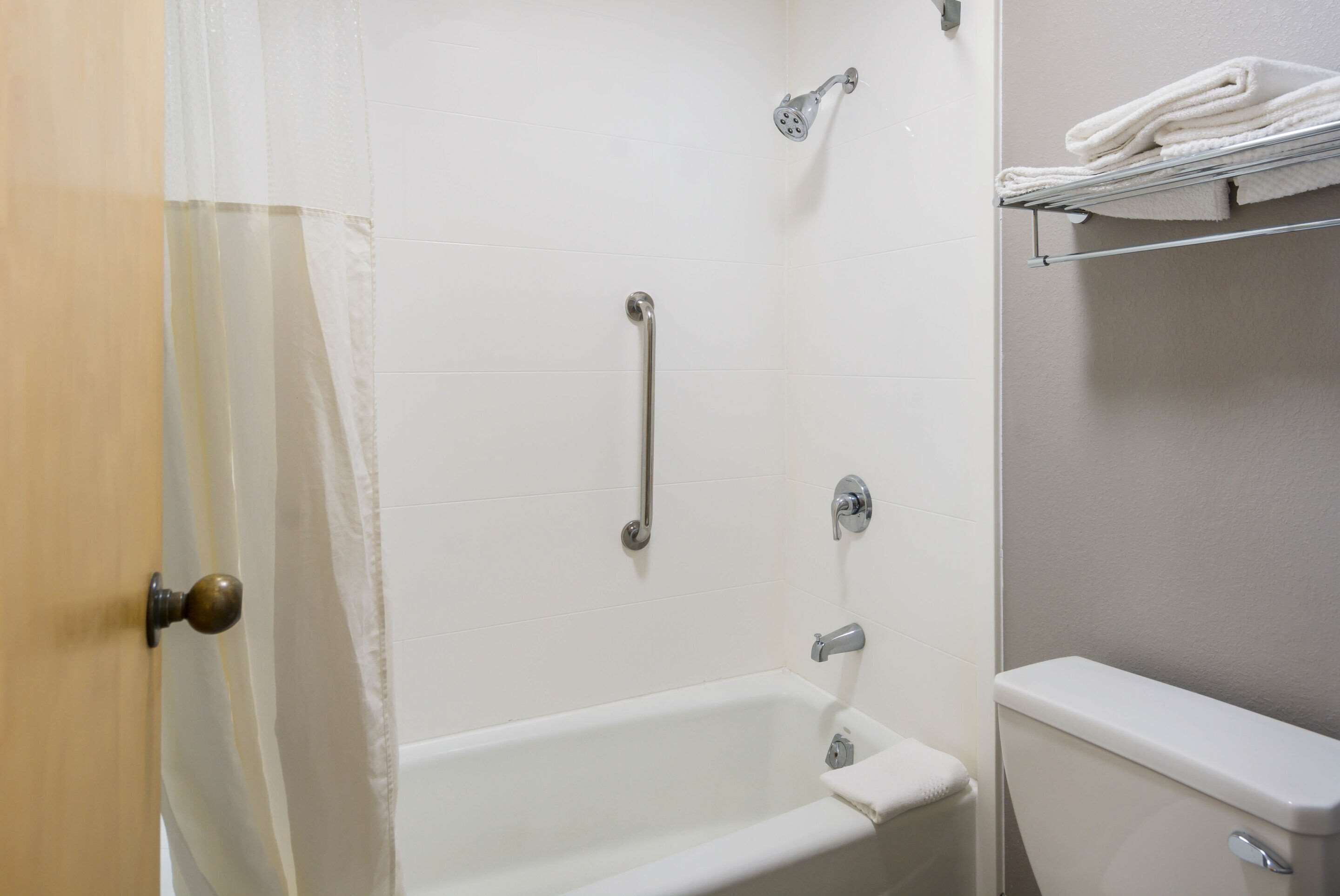 Un baño con bañera, inodoro, ducha con cabezal de ducha manual y un perchero para toallas.