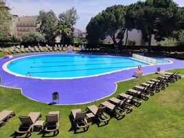 A large outdoor swimming pool with multiple lanes, surrounded by lounge chairs and a grassy area.