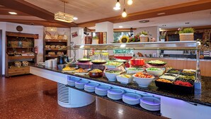 Zona de buffet amb diferents opcions de menjar, un espai de begudes a disposició del client i una barra amb plats i draps de paper.