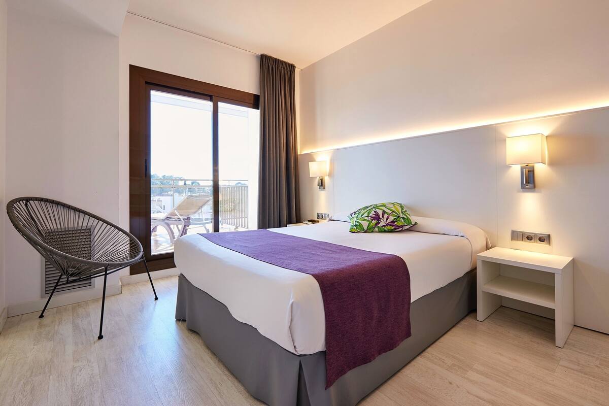 Hotellihuone, jossa on sänky, tuoli, yöpöytä ja näkymä kaupunkiin.