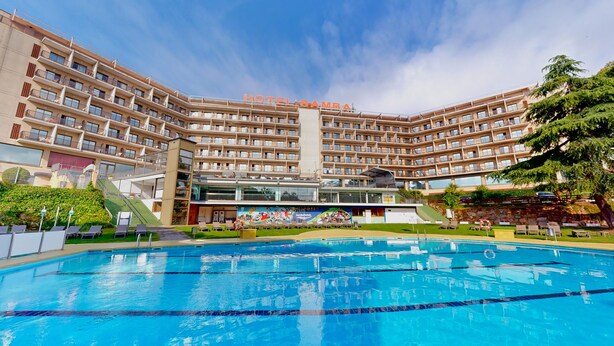 Un hotel amb diversos balcons, una piscina i un cel serè.