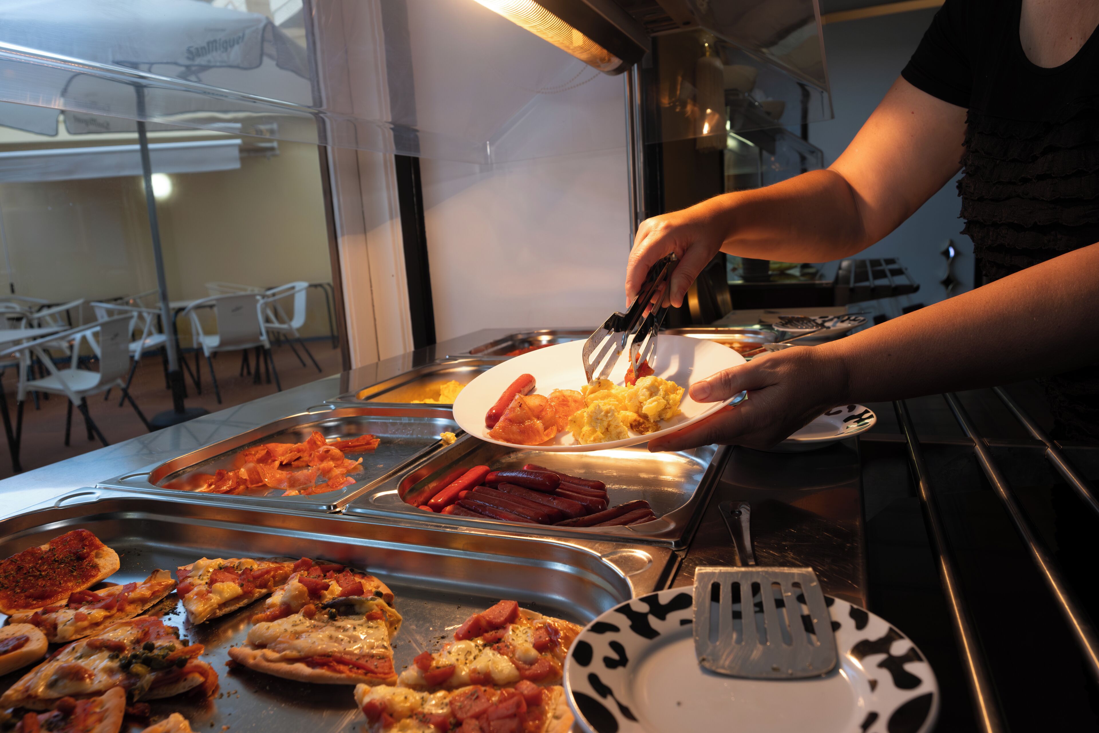 Un bufé con diversas opciones de comida y una persona sirviendo.