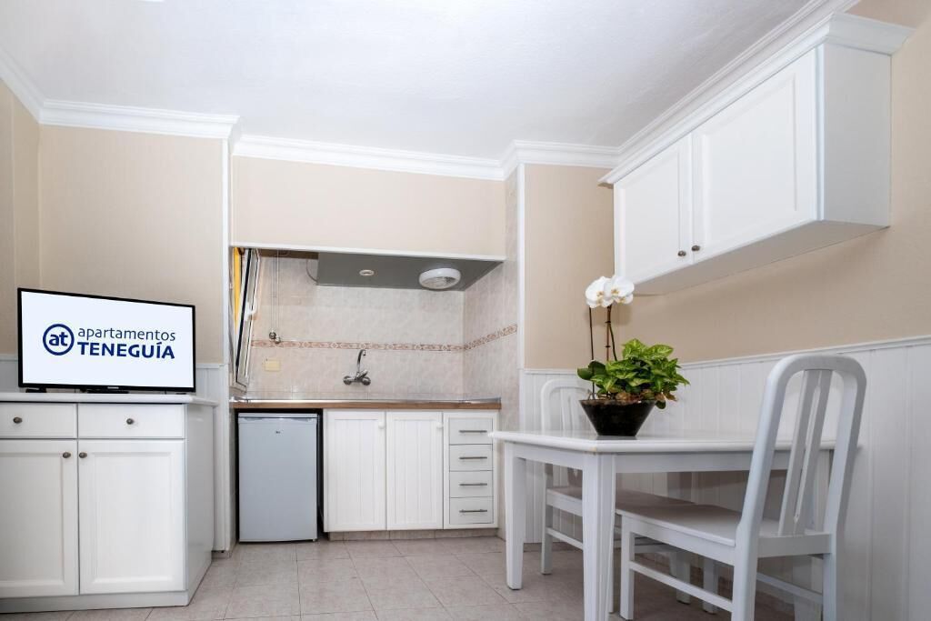 A small kitchen with white cabinets, a sink, and a dining area with a table and chairs.
