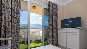 A hotel room with a balcony, a TV on a cabinet, and a view of the city.