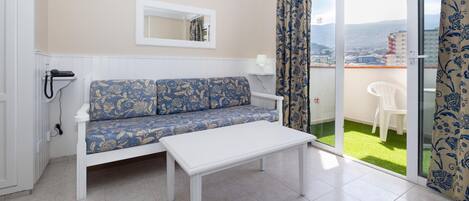 A room with a sofa, a table, a mirror, and a balcony with a view.