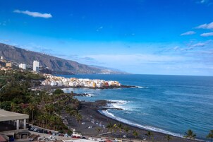 A coastal town with buildings along the beach, a clear sky, and a view of the ocean.