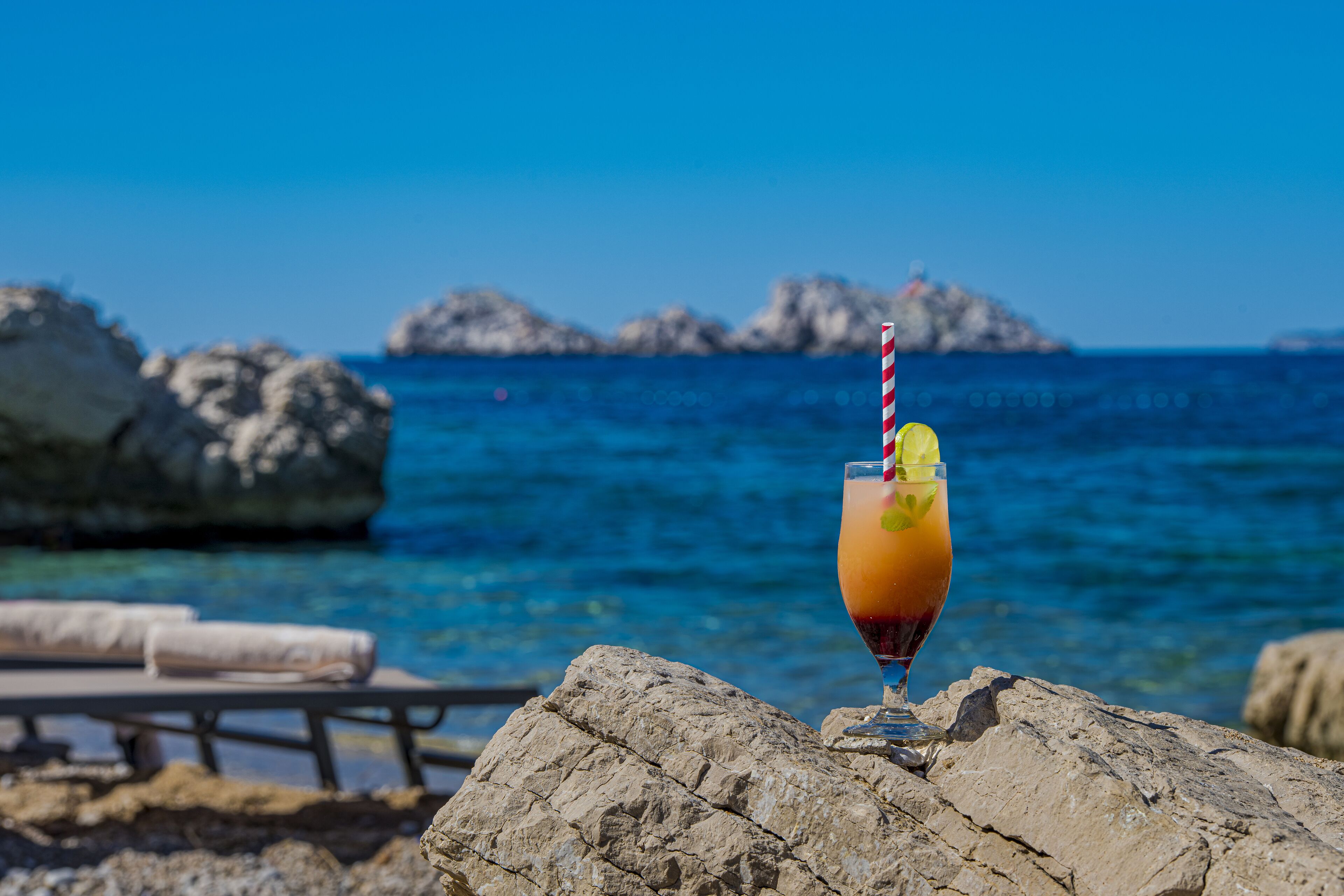 Ein Getränk in einem Glas auf einem Felsen mit Blick auf das Meer und Felsen im Hintergrund.