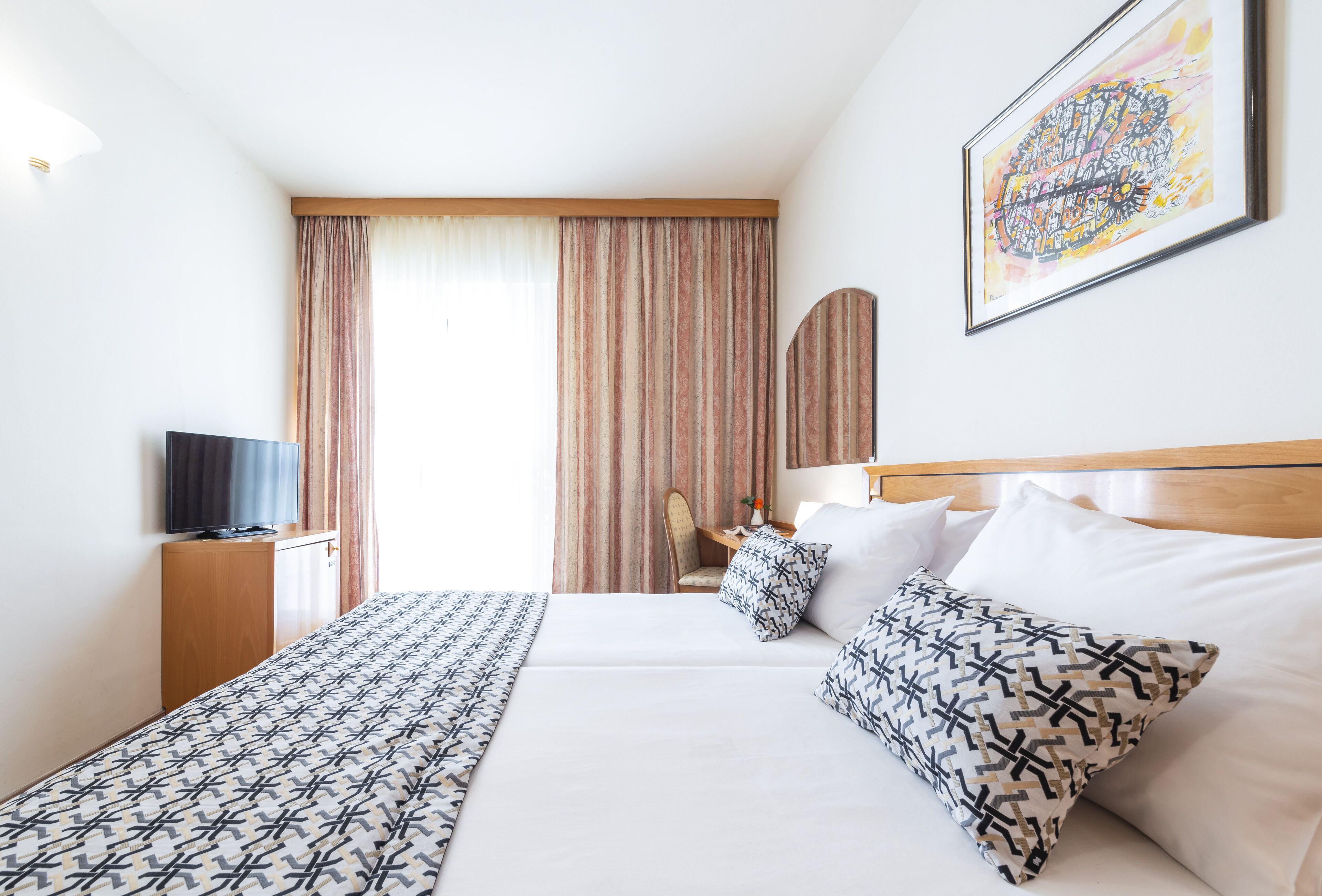 A hotel room with a bed, a television, a desk, and a chair.