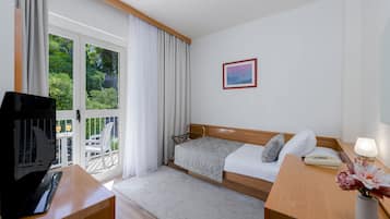 Une chambre d’hôtel avec un lit, un bureau avec un ordinateur, une chaise, une télévision, une fenêtre avec des rideaux et un tableau au mur.