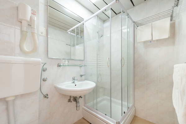 Un baño moderno con ducha acristalada, lavamanos blanco y barra para toallas.