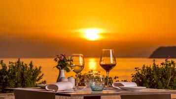 A table set for two with wine glasses and a vase of flowers, overlooking a sunset over the water.