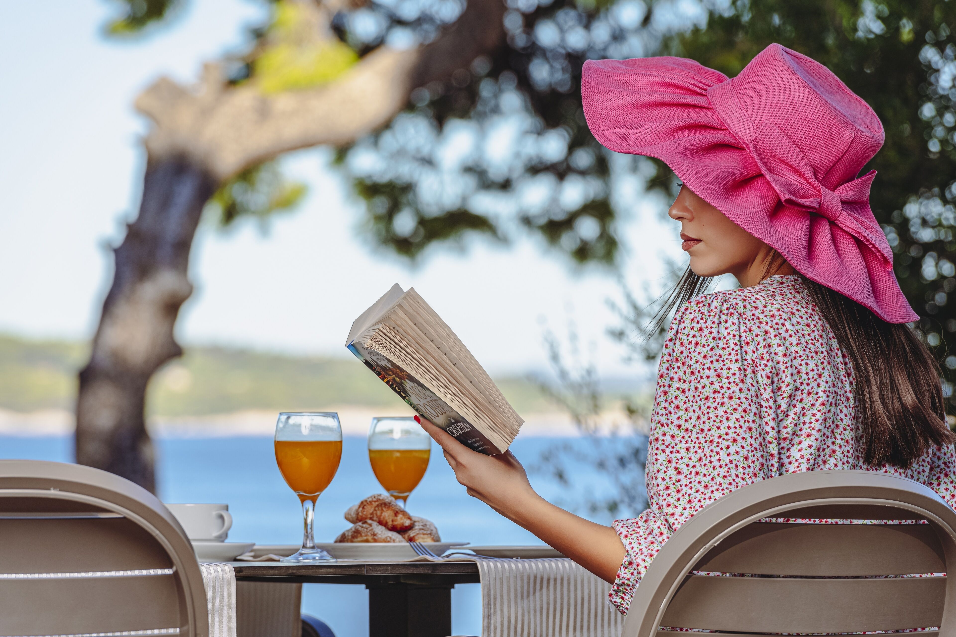 Eine Person liest ein Buch an einem Tisch im Freien mit Blick auf das Meer.
