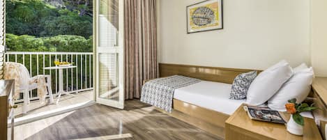 Hotelkamer met een bed, een tafeltje met een vaas, een stoel en een balkon met uitzicht op groen.