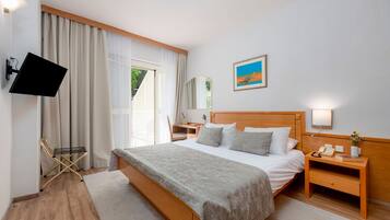 Une chambre d’hôtel avec un grand lit, une table de chevet avec une lampe, un téléviseur fixé au mur et une fenêtre avec des rideaux.