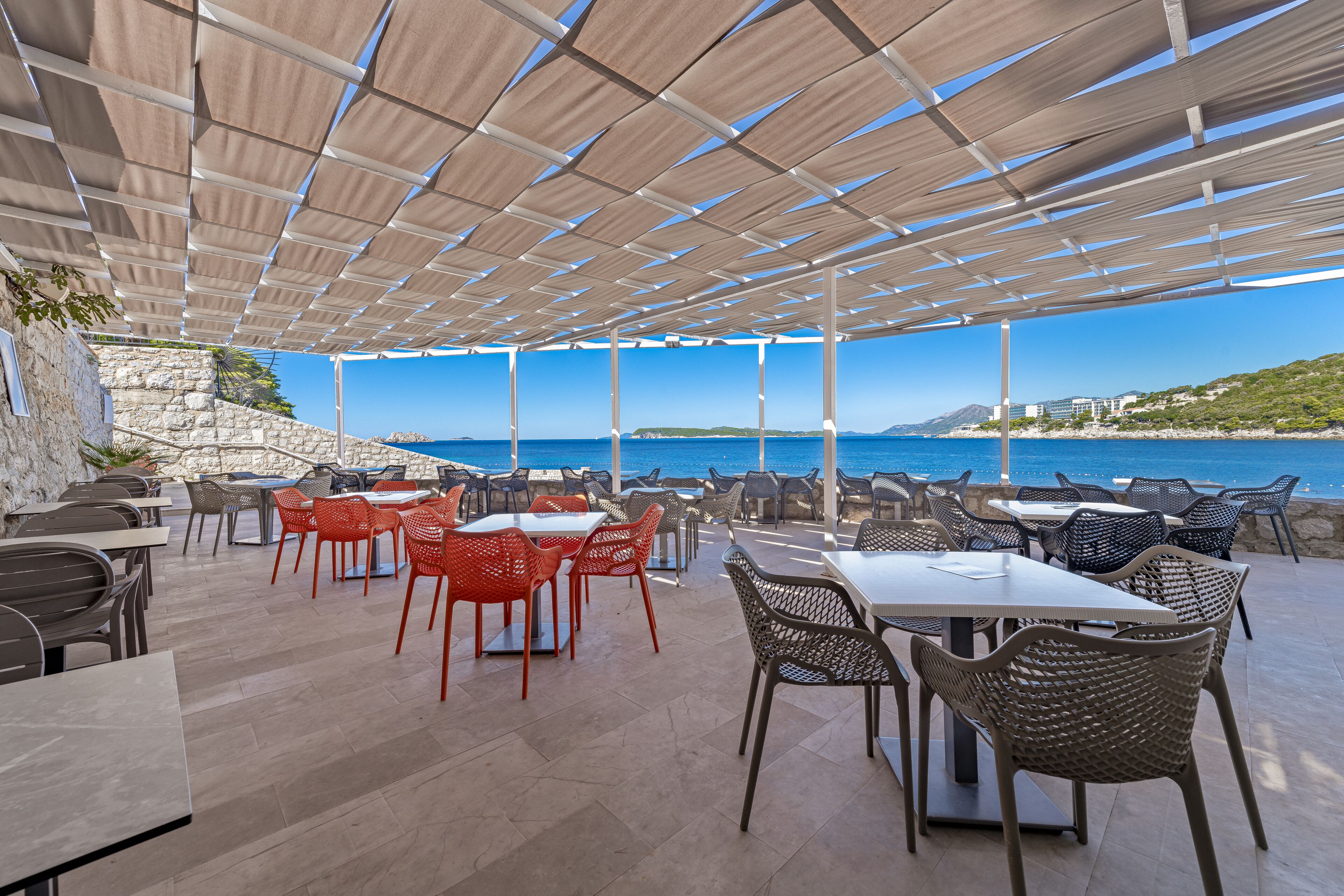 Un espacio de comedor al aire libre con mesas y sillas, con vistas a la costa.