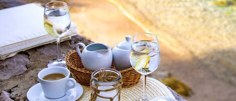 A table set with a cup of coffee, a glass of water, a glass of wine, a small jar, and a teapot on a woven mat.