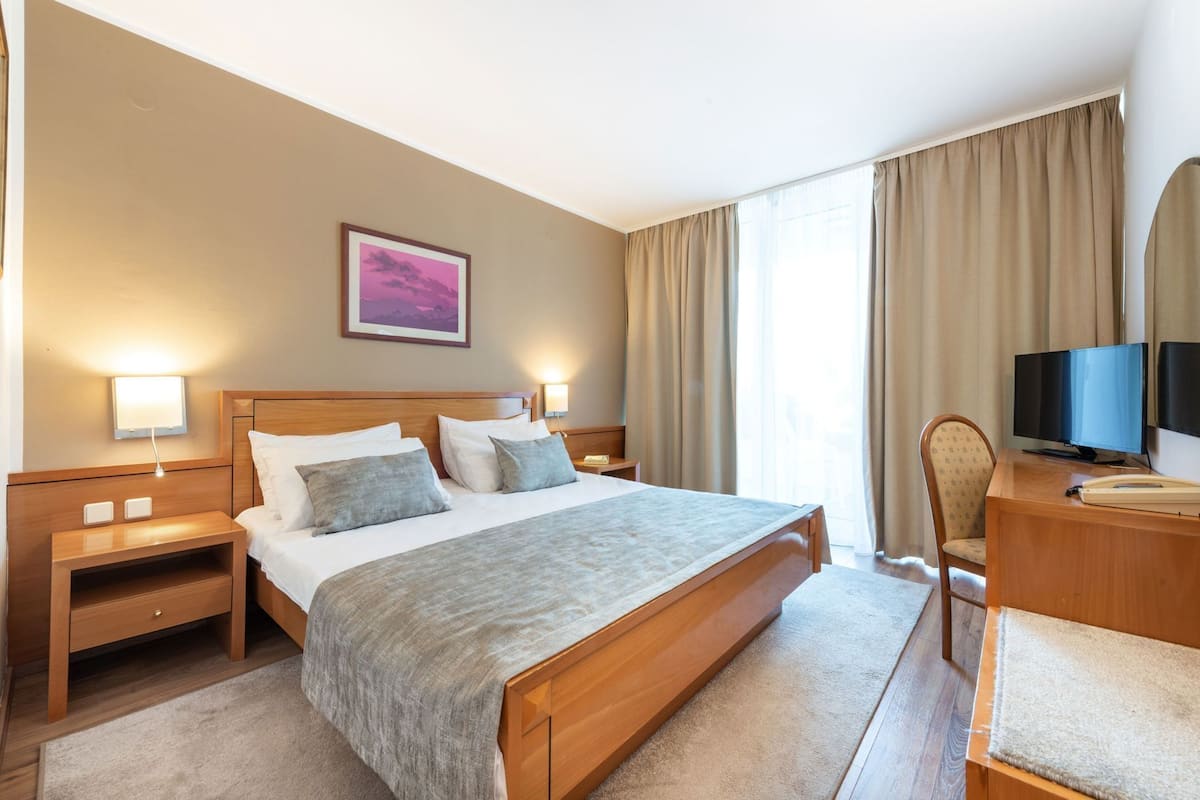 A hotel room with a bed, bedside lamps, a desk with a TV, and a chair.