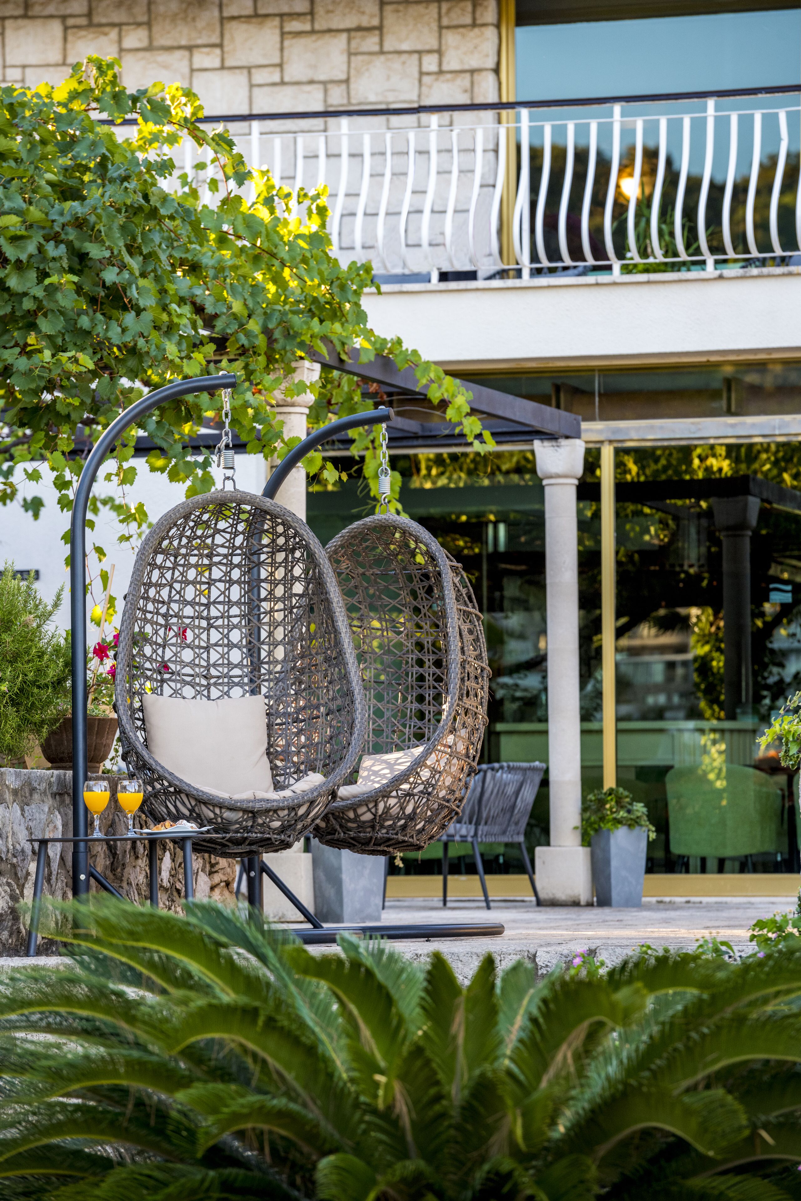 Two wicker chairs with cushions, a stone wall, and a balcony with a railing.