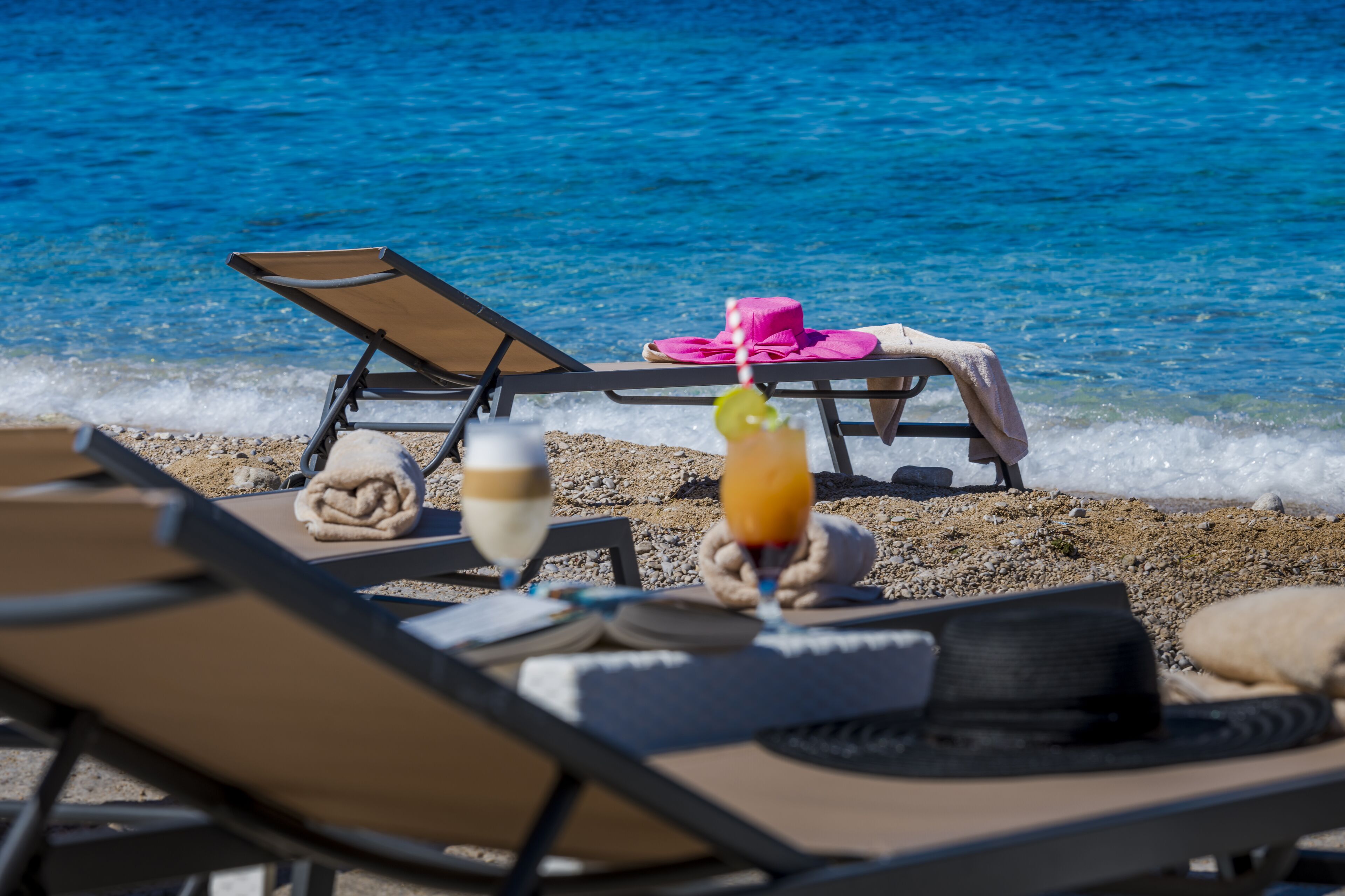 A beachside lounge with sun loungers, a drink, and a hat on the sand.